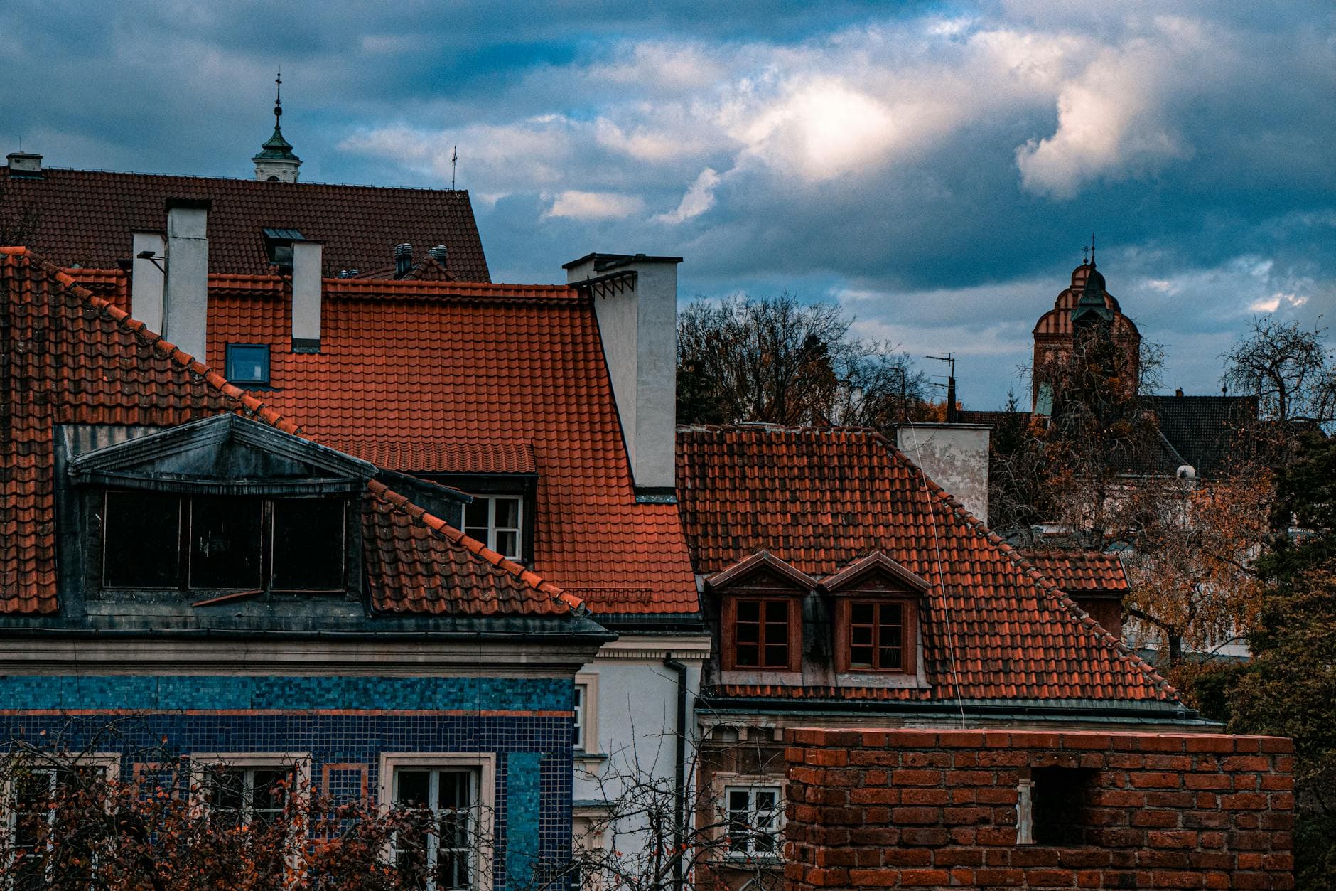 View of rustic rooftops in Warsaw's old town during autumn, framed by cloudy skies.